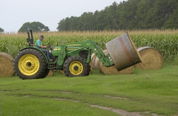 A man uses a farm machine to move a bale of hay. 