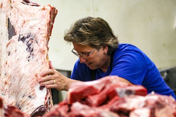 A person works behind a pile of red meat.