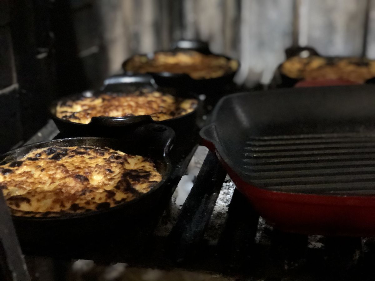 Three cast iron pots filled with charred cheese next to red cast iron grill pan