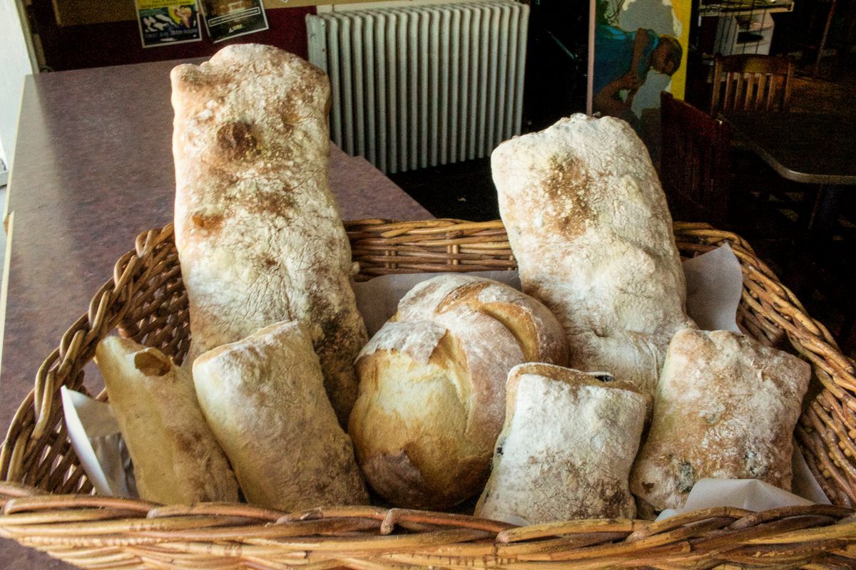 A basket filled with flour dusted bread loaves of different shapes and sizes.