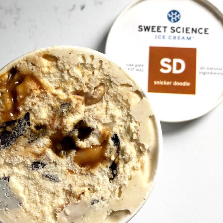 A white pint container of Sweet Science ice cream has nouget-colored ice cream with a molten core of caramel, chocolate bits, with a few peanuts wedged into the mix