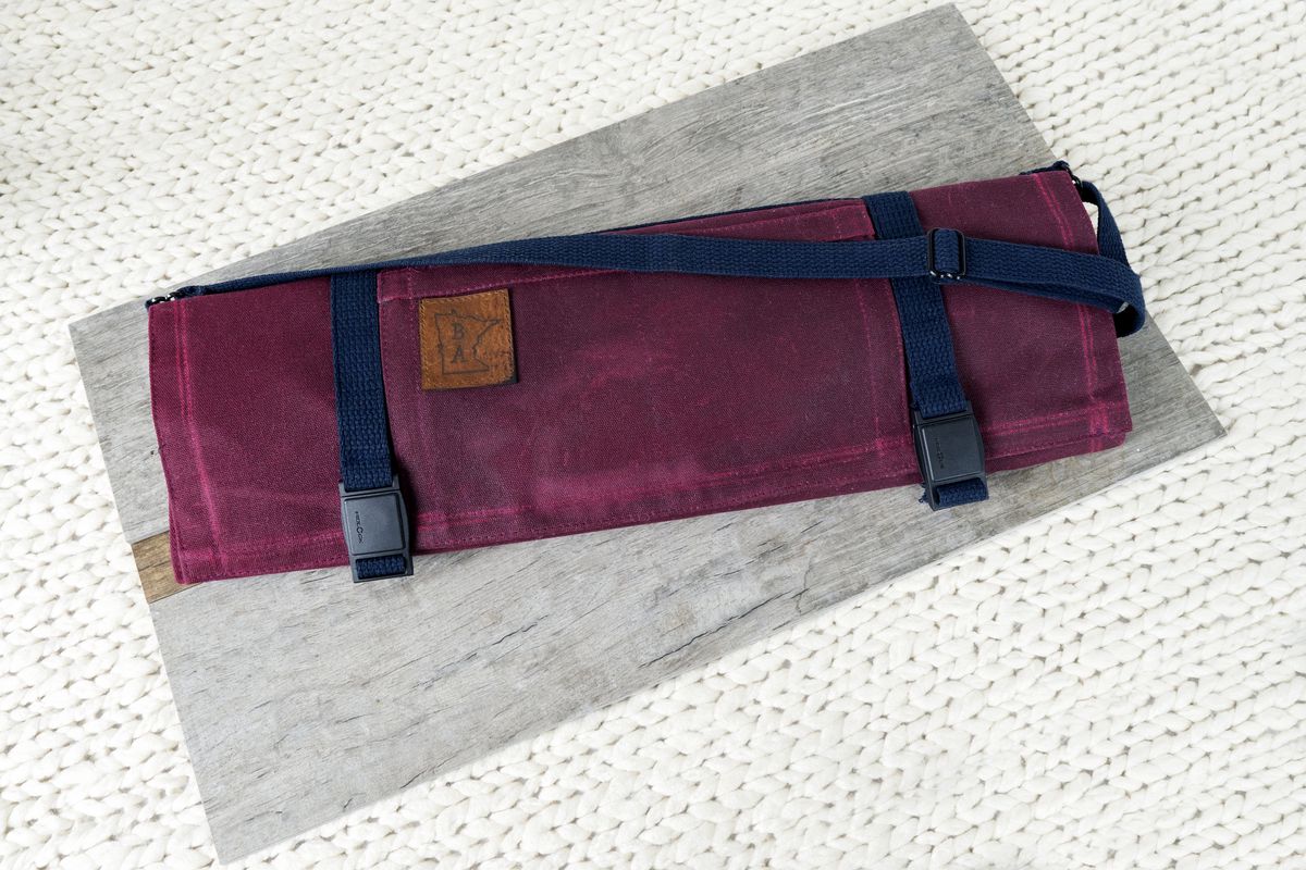 A magenta colored knife roll with navy straps and details