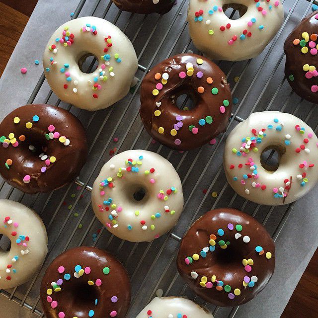 A tray of doughnuts frosted with white and chocolate, decorated with multi-colored sprinkles