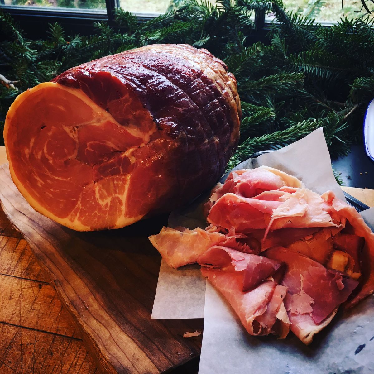 A smoked ham sliced, surrounded by green fur branches
