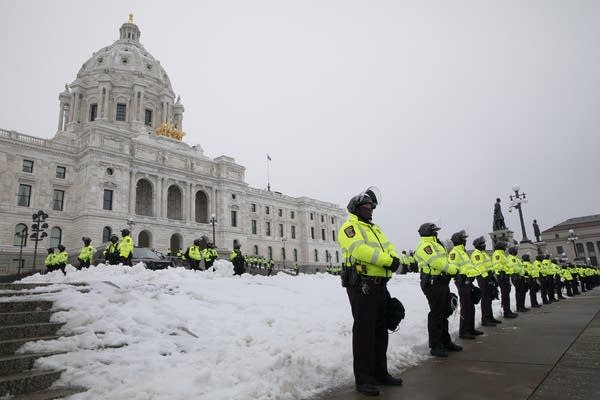 Law enforcement stand in a line in front of a capitol building. 