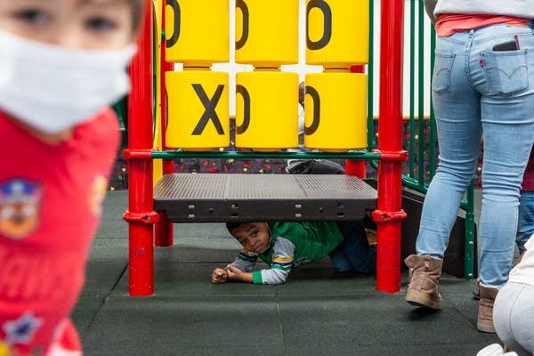 A young boy hides under a playground platform.