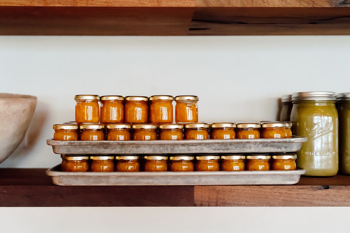 Three rows stacked up of small red condiment jars with gold lids on a wooden shelf.
