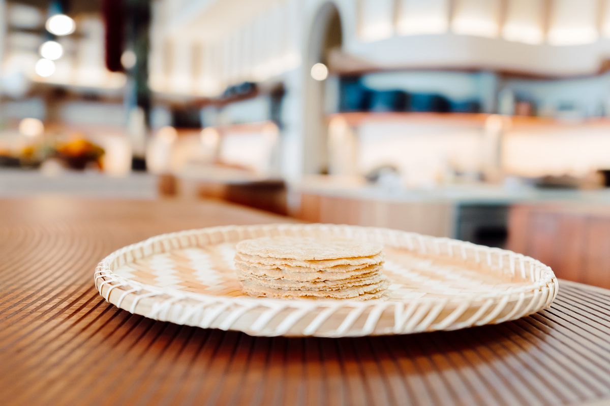Pale yellow tortillas stacked on a wide, flat basket.