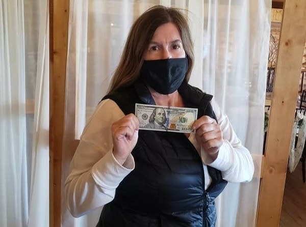 A woman in a mask holds a $100 bill. 