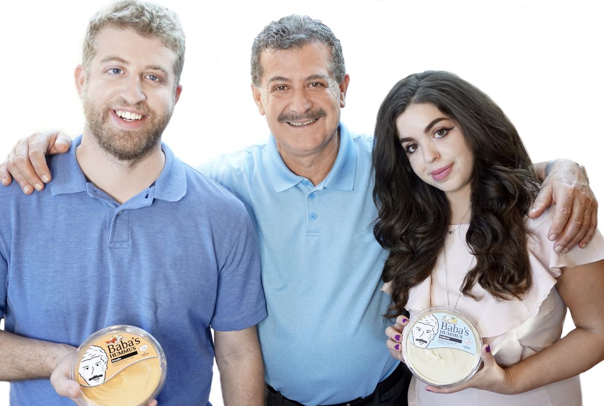 Son, father, and daughter pose on a white background. The adult children on either end, hold containers of hummus