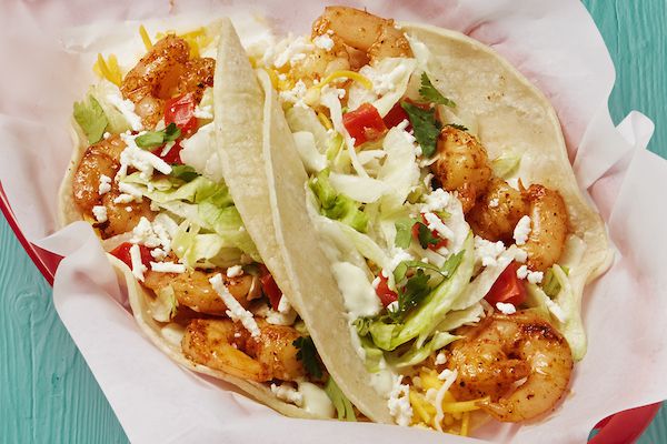 A highly-saturated close up of shrimp tacos in flour tortillas with shredded lettuce, tomatoes, and crumbled cheese
