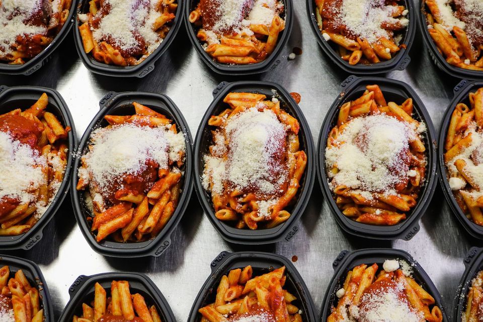 Lines of black takeout containers full of Cosseta’s penne in red sauce with a heft scoop of parmesan crumbles on top