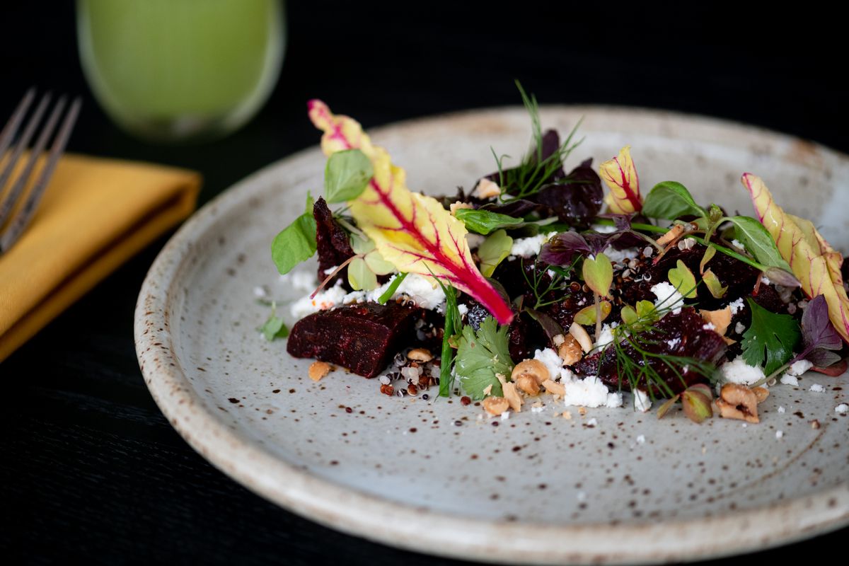Centered in the middle of a gray, mottled stone plate are a line of dark beets tossed with crumbled white cheese, micro herbs, and nuts