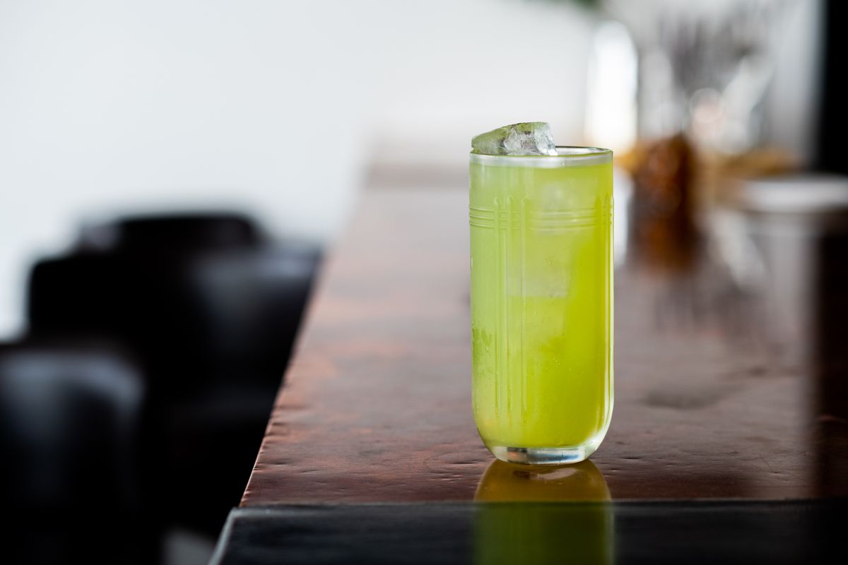 A light green colored drink in a tall glass filled with ice set at the end of the bar.