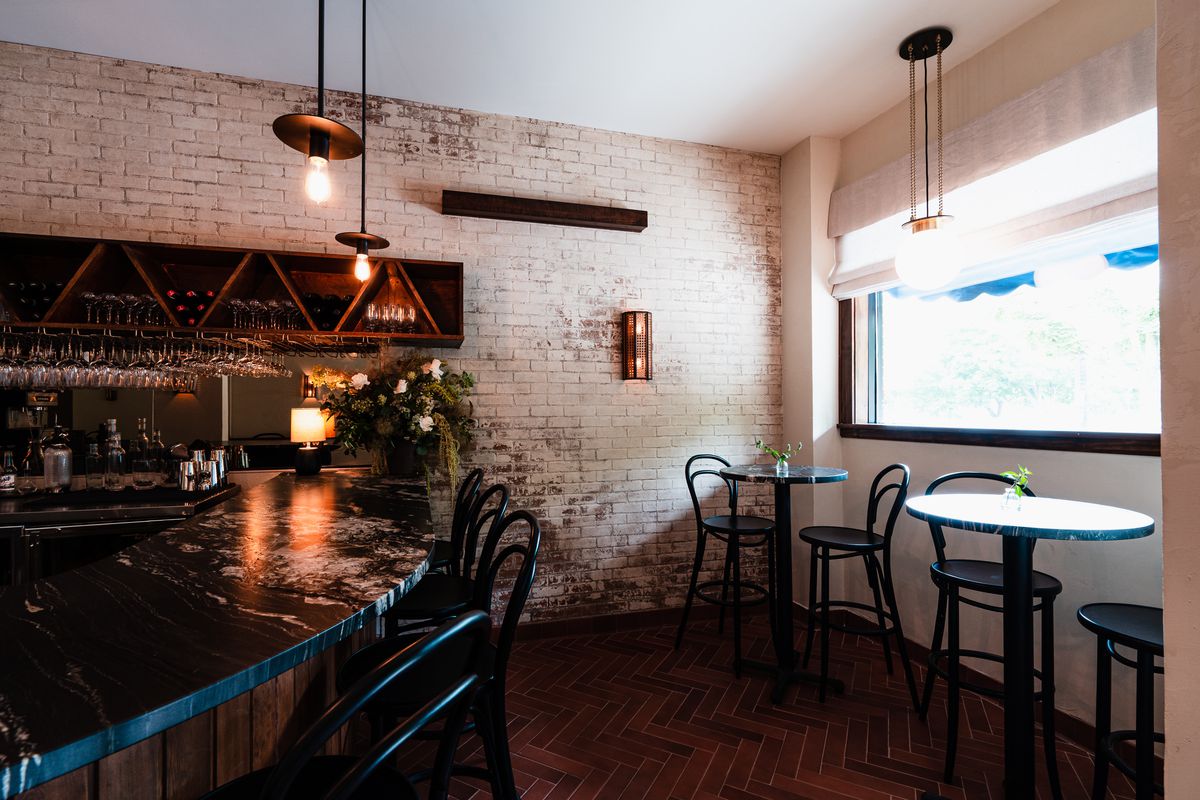 The bar space in Myriel is small, lined by brick walls with two tall two-top tables by the front window, and a curved stone bar lined by tall, black bar seats. All the fixtures behind the bar are a dark wood, giving the whole space a rustic European feel.