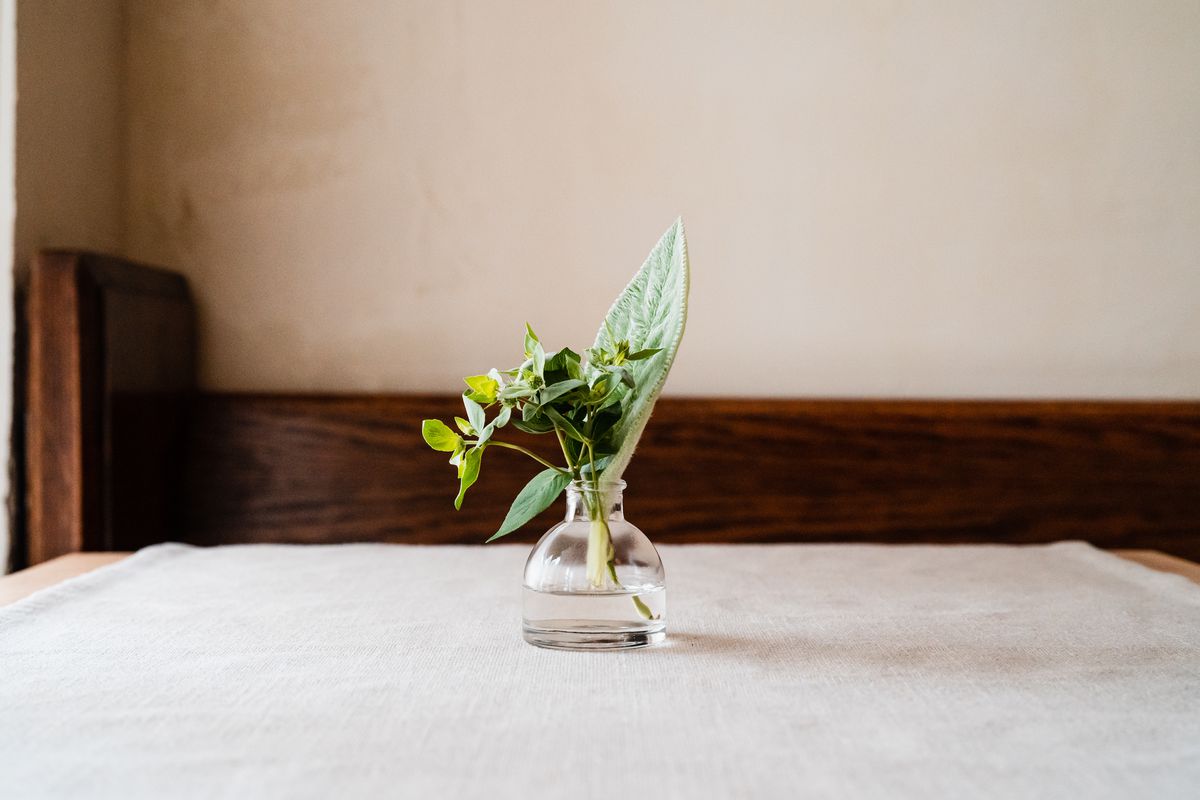 A table top with a cream tablecloth and a small vase with cut leaves inside it.