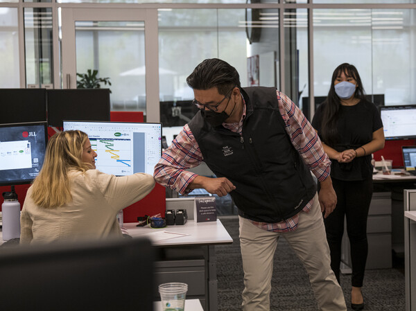 Employees elbow bump at a JLL office in Menlo Park, Calif., last September. With the delta variant surging, mask mandates are returning and some employers are now requiring employees to be vaccinated before coming to the office.