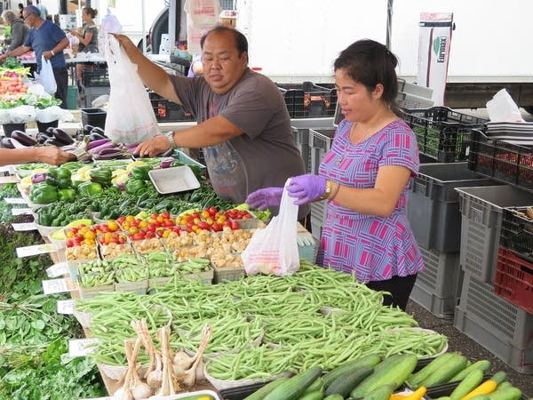 Two people sell vegetables at a farmer's market. 