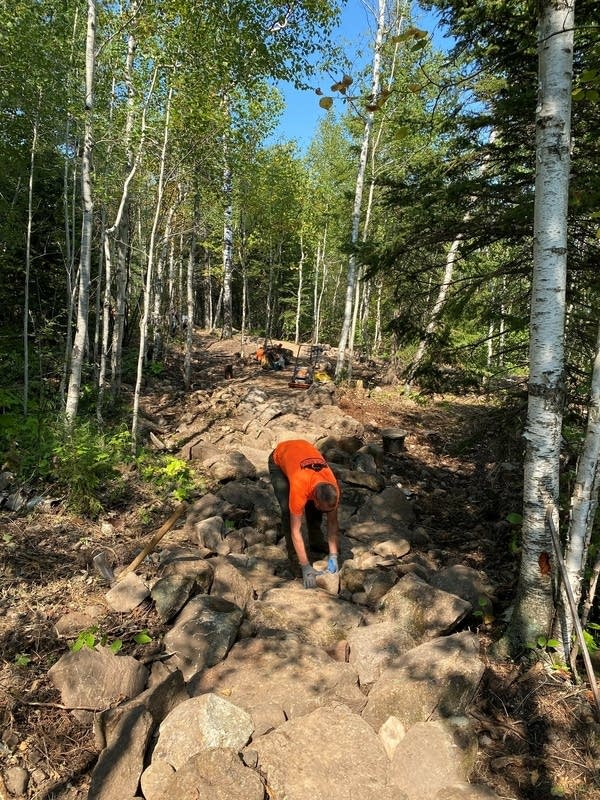 A builder places a rock on a bike trail. 