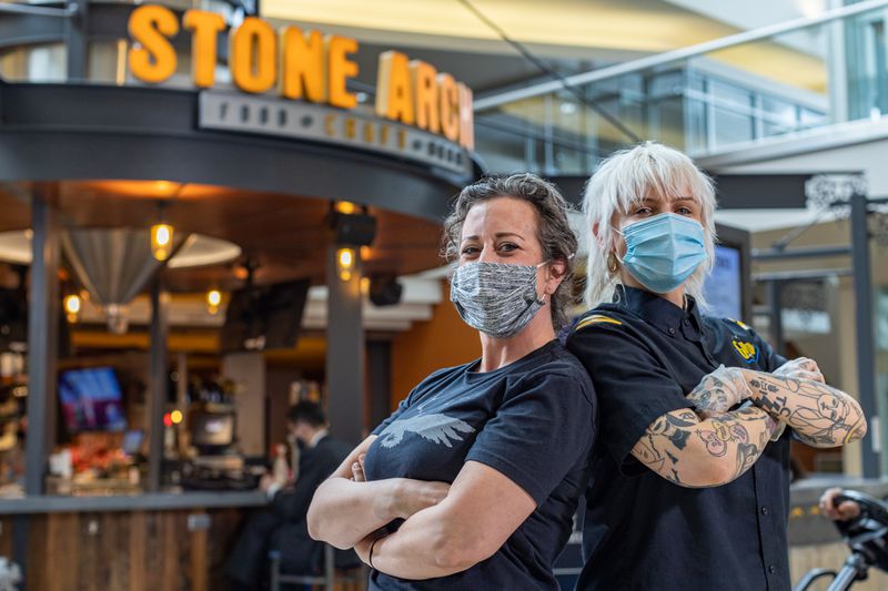 Two employees wearing masks outside of Stone Arch’s signage.