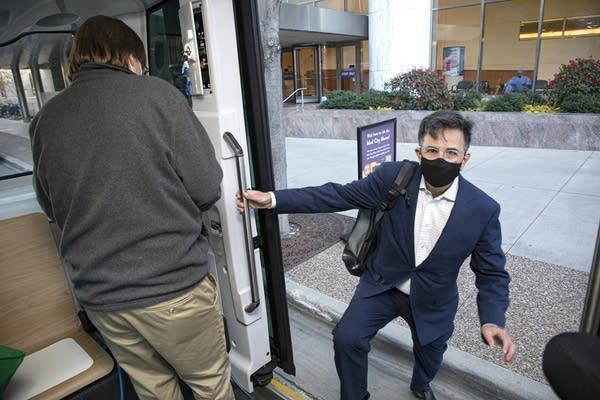 A person in a suit and face mask boards the vehicle