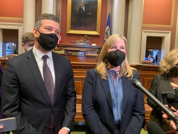 Two people in masks talk to reporters.