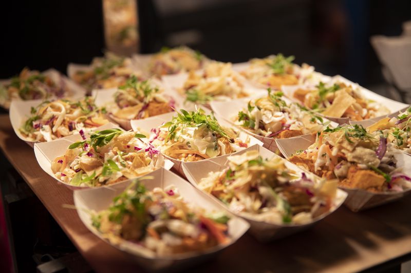 Paper boats filled with chicken tikka, rice, slaw, and veggies on a wooden board. 