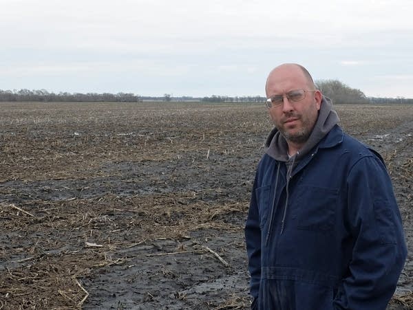 A man stands next to a muddy farm field