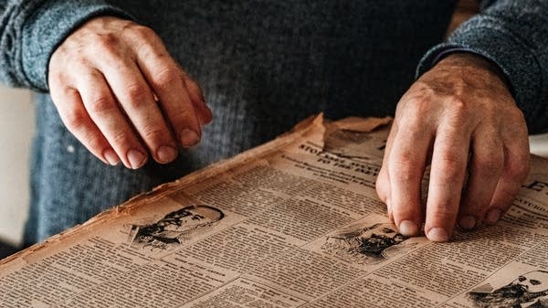 Two hands inspect an aging newspaper.