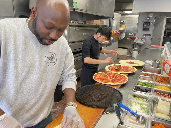 Owner Joseph Charles and an employee prepare pizzas for delivery to a nearby business. but orders are way down he says, since inflation has driven prices up.