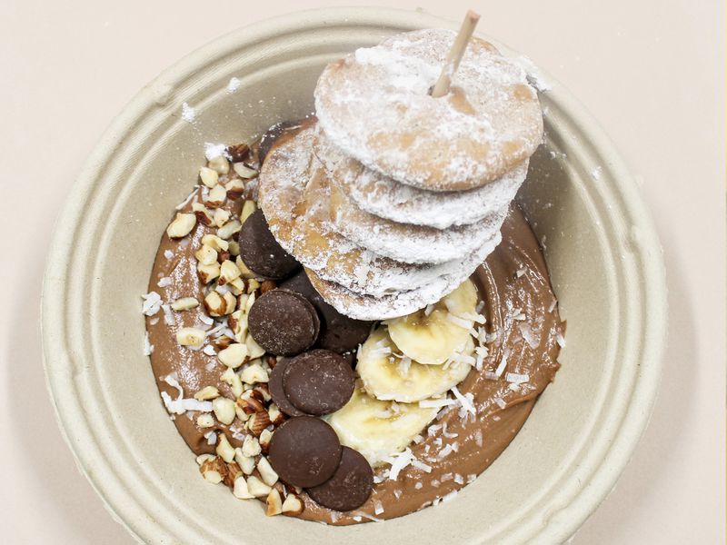 A beige bowl with creamy chocolate hummus topped with bananas, chocolate chips, and disks of pita bread dusted in powdered sugar. 