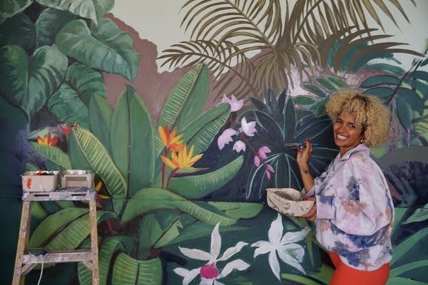 A person smiles while painting colorful plants on a wall.