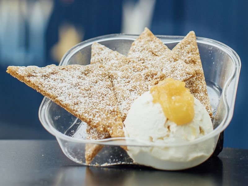 Triangular pieces of cookie and corn-chip hybrid dusted with powdered sugar beside a scoop of ice cream topped with lemon curd. 