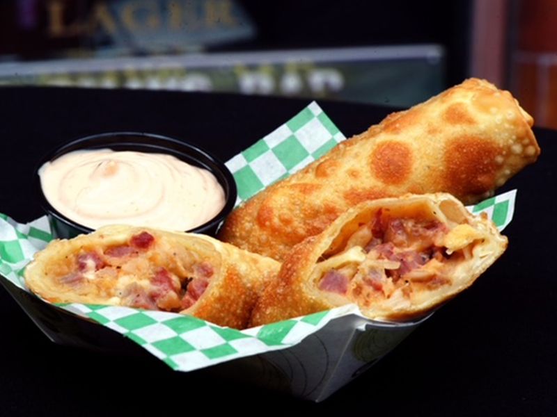 A deep fried egg roll with corned beef, cheese, and sauerkraut filling and a small dish of Thousand Island Dressing. 