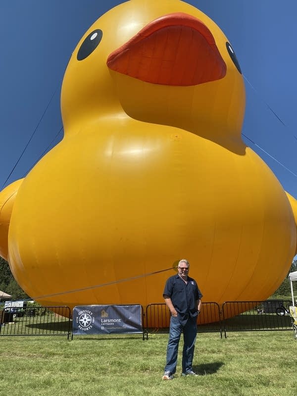A man stands in front of a large rubber duck