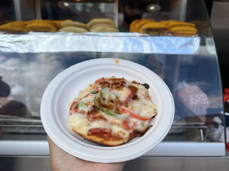 A hand holds a mini pizza with chicken and peppers on a white plate. 