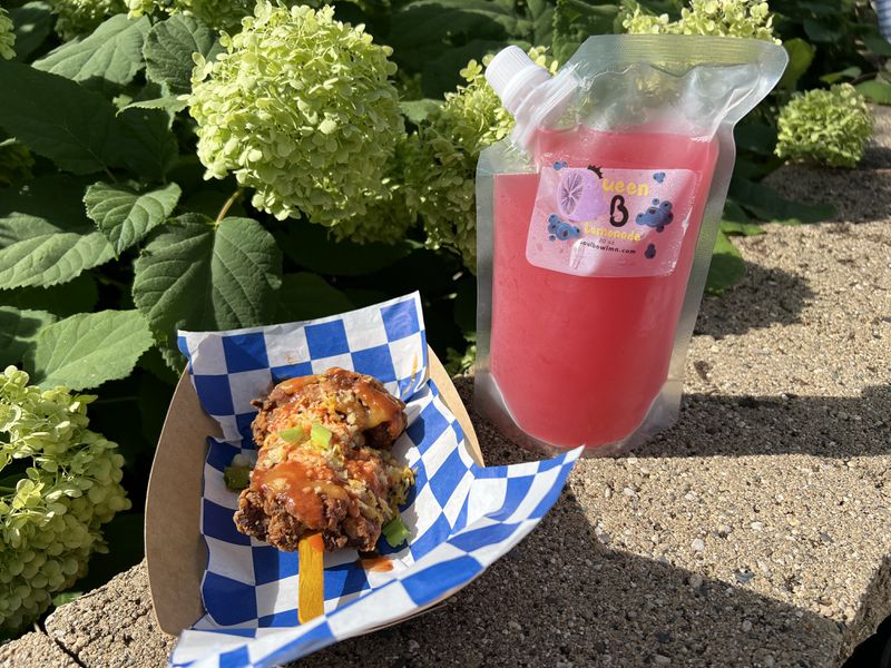 A basket with fried chicken on a stick and a pouch of pink lemonade. 