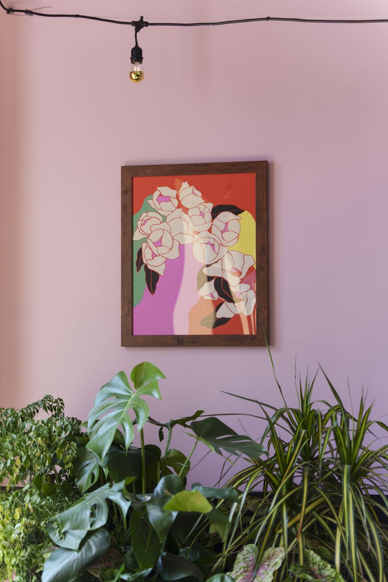 A pink wall with a piece of artwork and greenery in the foreground. 