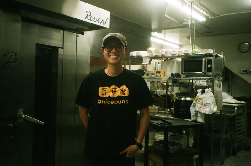 Michelle Kwan, wearing a black and yellow T-shirt that reads “#nicebuns.” stands in Keefer Court’s industrial kitchen. 