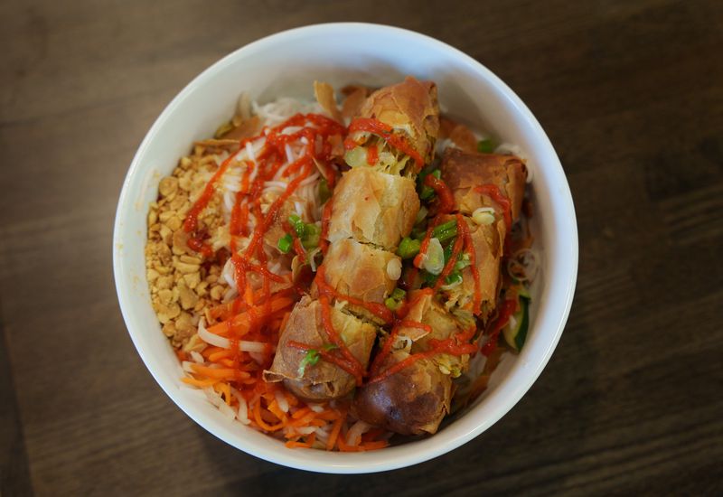 Egg rolls sit on a bed of rice noodles, shredded carrots, and peanuts. 