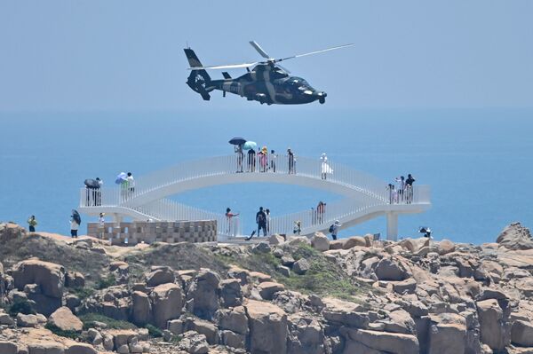 Tourists look on as a Chinese military helicopter flies past Pingtan Island, one of mainland China's closest points to Taiwan, in Fujian province on Aug. 4, ahead of Chinese military drills off Taiwan following House Speaker Nancy Pelosi's visit to the self-ruled island.