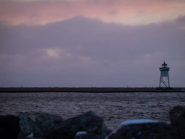 A lighthouse is framed below a pink cloudy sky