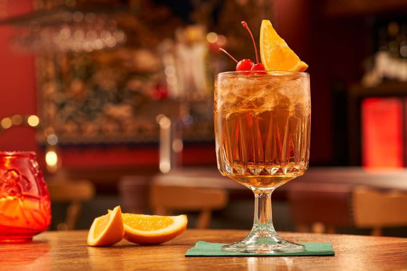 A Wisconsin-style Old Fashioned sitting on a table, garnished with maraschino cherries and an orange slice. 