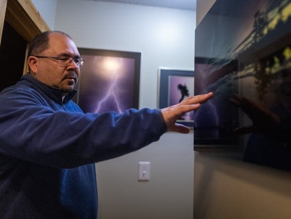 A man gestures at a hanging photograph in a hallway