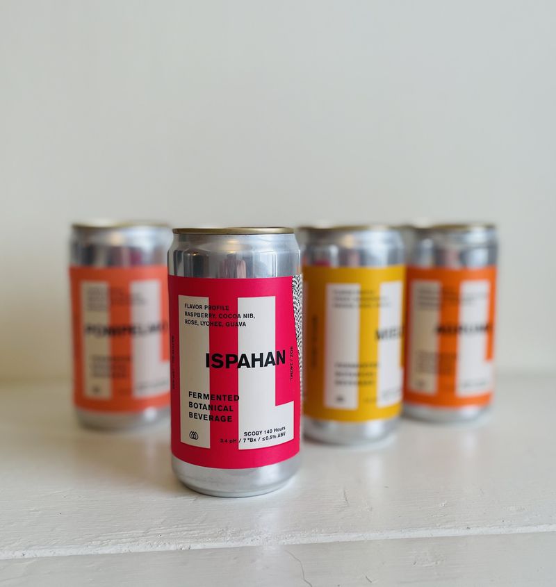 Four small aluminum cans with orange, yellow, and pink labels against a white background. 