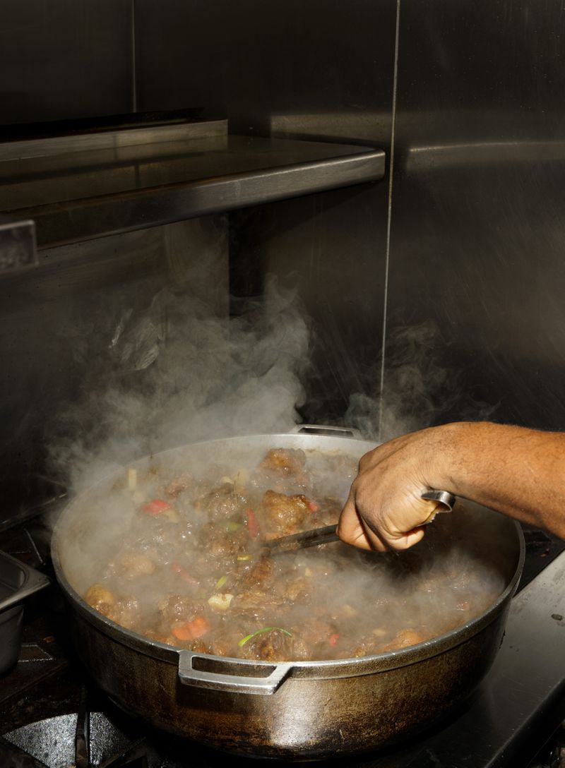 A hand stirring a large steamy pot of oxtail stew.