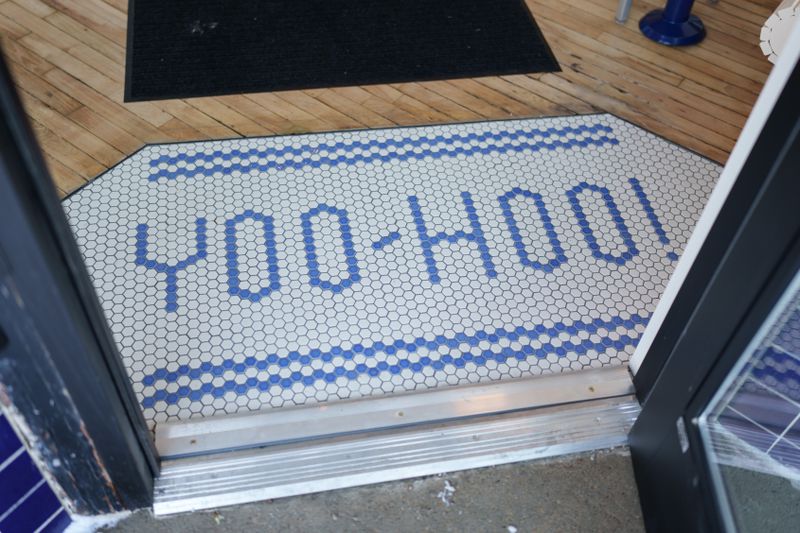 Blue and white tiling on the floor reading “Yoo-Hoo!”