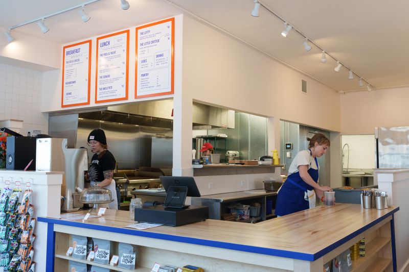 Martha Polacek behind a wooden counter with a deep blue stripe. An industrial kitchen in the background. 