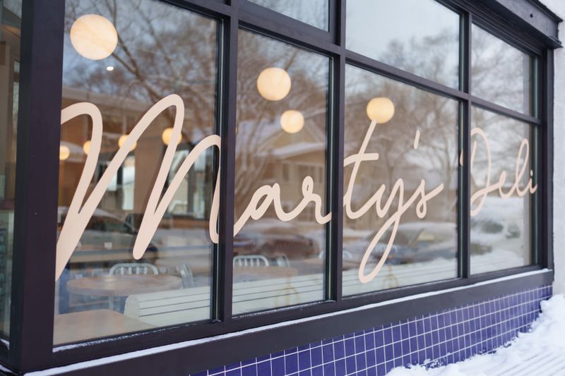 Storefront windows above blue tiling with a decal reading “Marty’s Deli.”