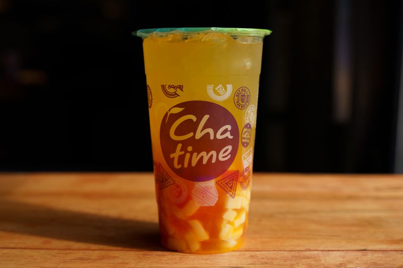 A plastic cup of orange liquid with little yellow cubes of jello in the bottom.